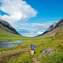 Vandrare på stig i en grön dalgång med sjö och fjäll. Syterskalet Hemavan bjuder på storslagen natur.