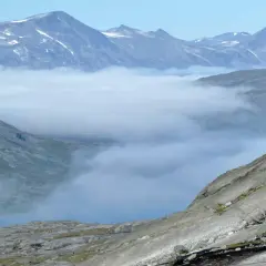 Moln sveper genom dalarna i Padjelanta nationalpark, med snöklädda bergstoppar som sticker upp ovanför.