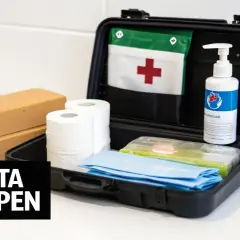 Första hjälpen-kit med plåster, kompresser, handsprit och en röd kors-flagga. Ett krispaket mat kan vara bra att ha.