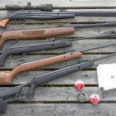 En samling kraftigt luftvapen, ammunition och måltavlor ligger utspridda på trä.