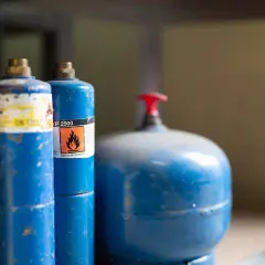 Blå gasflaskor, en med varningssymbol för brandfarlighet, redo att förvara bensin säkert.