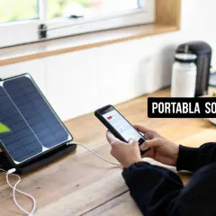 En kvinna laddar sin mobil med hjälp av bärbara solceller vid ett köksfönster.