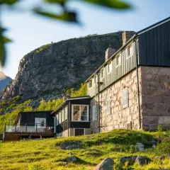 Boende Kebnekaise: sten- och träbyggnader med utsikt mot snöklädda berg. Grönskande sluttningar och solljus.