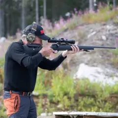Man med hörselskydd och keps siktar med ett Strasser RS700-gevär i skogen.