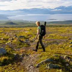 Vandrare med ryggsäck på väg mot Abisko turiststation, med fjäll och sjö i bakgrunden.
