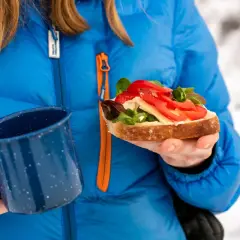 En person i blå jacka håller en smörgås och en mugg. En mysig stund med värme i bilen på vintern.