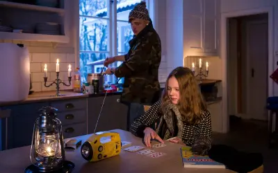 Två personer i ett kök med levande ljus och en sprit kamin. En flicka spelar kort vid ett bord, medan en person lagar mat vid spisen.