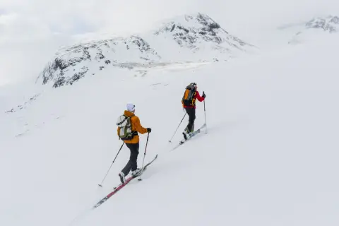 Två skidåkare på väg uppför ett snötäckt berg, en fantastisk sylarna topptur i fjällen.