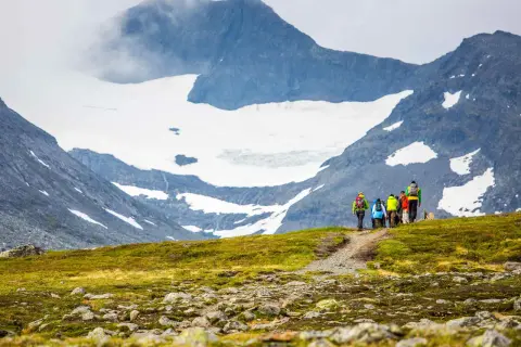 Vandrare på väg mot STF Sylarna, med glaciärklädda berg i bakgrunden.