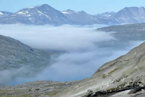 Moln sveper genom dalarna i Padjelanta nationalpark, med snöklädda bergstoppar som sticker upp ovanför.