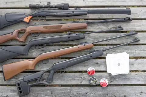 En samling kraftigt luftvapen, ammunition och måltavlor ligger utspridda på trä.