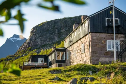 Boende Kebnekaise: sten- och träbyggnader med utsikt mot snöklädda berg. Grönskande sluttningar och solljus.