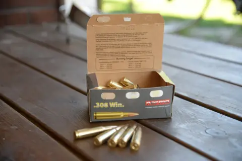 En öppen ask med .308 Win. ammunition på ett träbord. Texten på asken ger information om hur mycket ammunition man får ha hemma och dess användning.