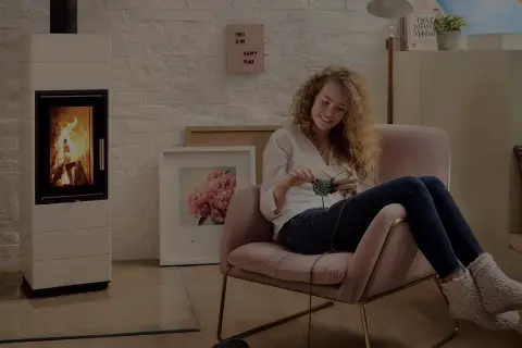 En kvinna stickar i en mysig fåtölj bredvid en modern gasol öppen spis.