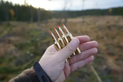 Hand håller fyra Norma Ecostrike 308 kulor, redo för test i skogen.