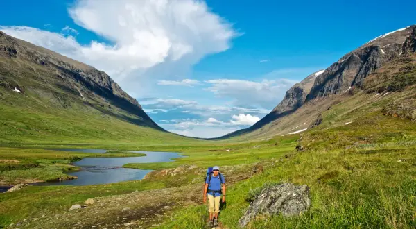 Vandrare på stig i en grön dalgång med sjö och fjäll. Syterskalet Hemavan bjuder på storslagen natur.