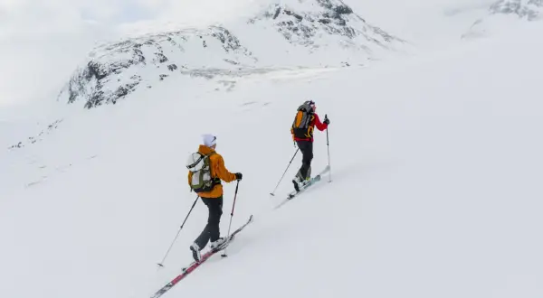 Två skidåkare på väg uppför ett snötäckt berg, en fantastisk sylarna topptur i fjällen.