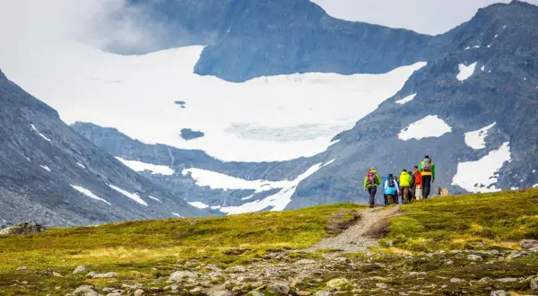 Vandrare på väg mot STF Sylarna, med glaciärklädda berg i bakgrunden.