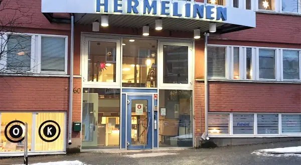 Byggnaden "HERMELINEN" med stora fönster och tegelväggar. En skylt med "Fotvård" syns. Trots namnet är denna hermelin inte farlig, bara en byggnad.