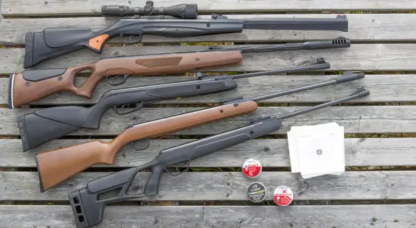 En samling kraftigt luftvapen, ammunition och måltavlor ligger utspridda på trä.