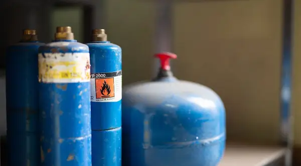 Blå gasflaskor, en med varningssymbol för brandfarlighet, redo att förvara bensin säkert.