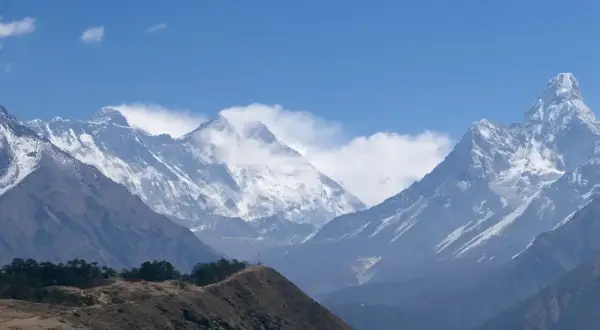 Majestätiska snöklädda bergstoppar i Nepal, med en kulle i förgrunden. En dröm om att vandra i Nepal.