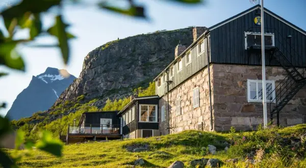 Boende Kebnekaise: sten- och träbyggnader med utsikt mot snöklädda berg. Grönskande sluttningar och solljus.
