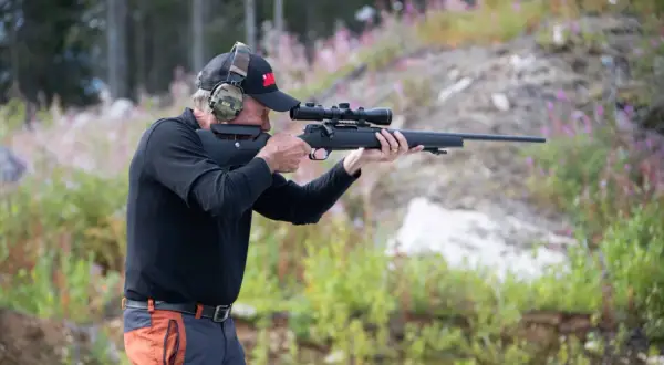 Man med hörselskydd och keps siktar med ett Strasser RS700-gevär i skogen.