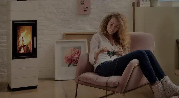 En kvinna stickar i en mysig fåtölj bredvid en modern gasol öppen spis.