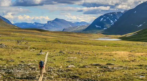 Vandrare på spång i Abisko-Nikkaluokta-landskap med berg och sjö.