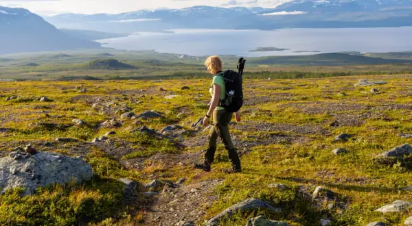 Vandrare med ryggsäck på väg mot Abisko turiststation, med fjäll och sjö i bakgrunden.