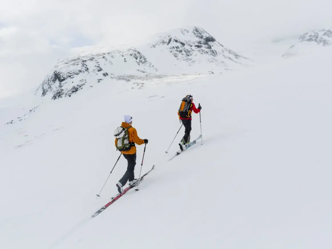 Två skidåkare på väg uppför ett snötäckt berg, en fantastisk sylarna topptur i fjällen.