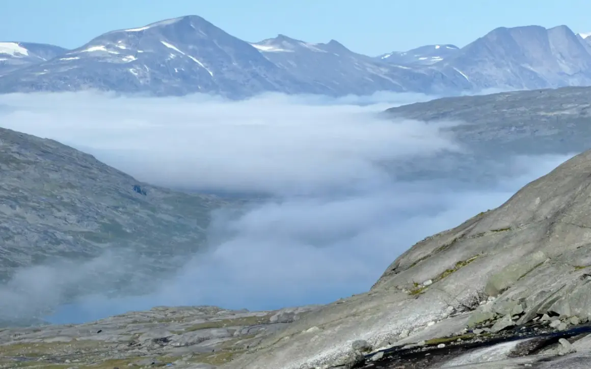 Moln sveper genom dalarna i Padjelanta nationalpark, med snöklädda bergstoppar som sticker upp ovanför.