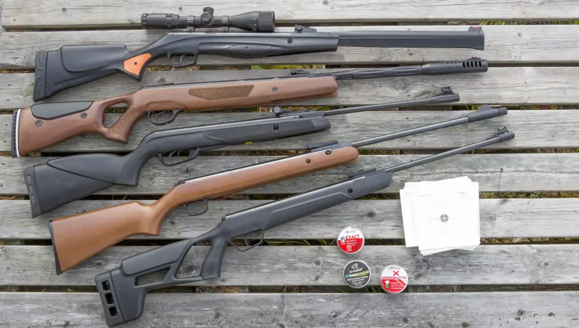 En samling kraftigt luftvapen, ammunition och måltavlor ligger utspridda på trä.
