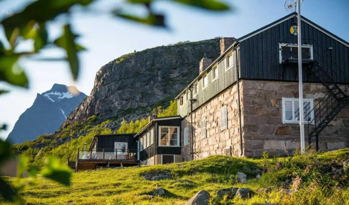 Boende Kebnekaise: sten- och träbyggnader med utsikt mot snöklädda berg. Grönskande sluttningar och solljus.