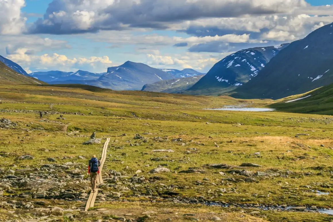 Vandrare på spång i Abisko-Nikkaluokta-landskap med berg och sjö.