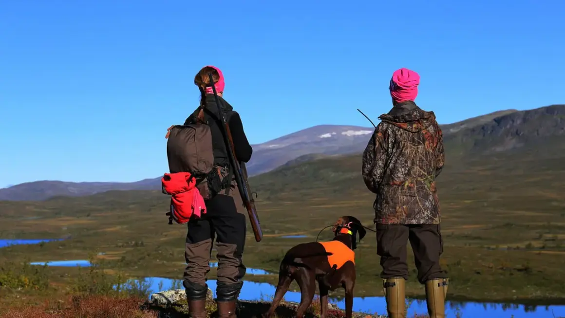 Två jägare med hund blickar ut över fjällandskap. En av dem har ett statligt jaktkort i fickan.