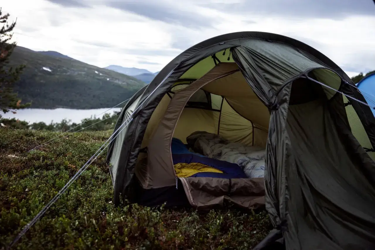 En gr&ouml;n t&auml;lt med sovs&auml;ckar redo f&ouml;r v&auml;rme i t&auml;lt utan el. Vacker utsikt &ouml;ver sj&ouml; och berg i bakgrunden.