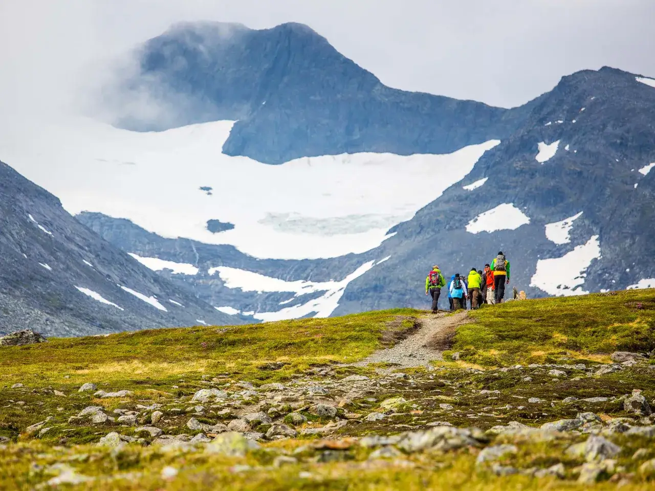 Vandrare på väg mot STF Sylarna med glaciärklädda berg i bakgrunden.