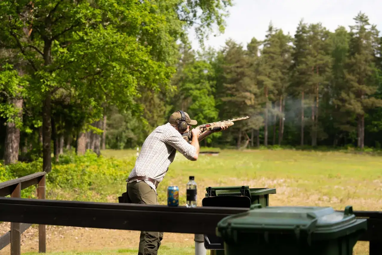 Man i h&ouml;rselskydd skjuter hagelgev&auml;r i form av lerduveskytte. R&ouml;k stiger fr&aring;n vapnet.
