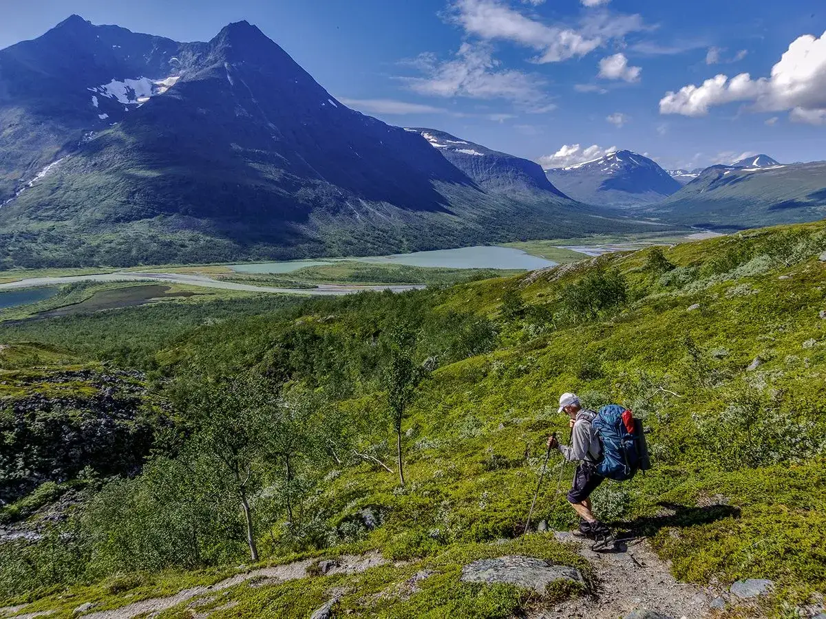 Vandrare med ryggsäck vandrar i Sarek nationalpark. Majestätiska berg och turkosa sjöar i bakgrunden.