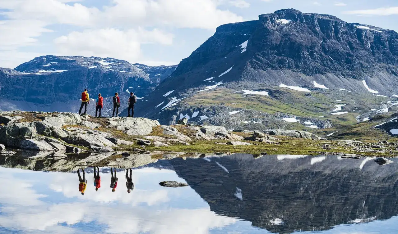 Vandrare njuter av midnattssol Sverige vid en spegelblank sjö med berg i bakgrunden.