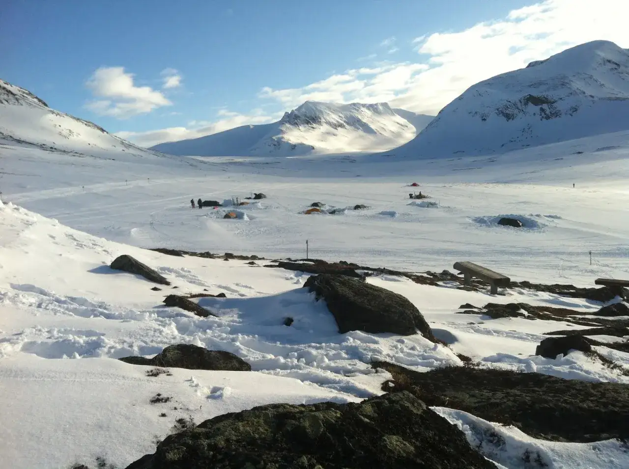 Vinterlandskap med tältläger och snöklädda berg. En grupp människor förbereder sig för en sylarna topptur.