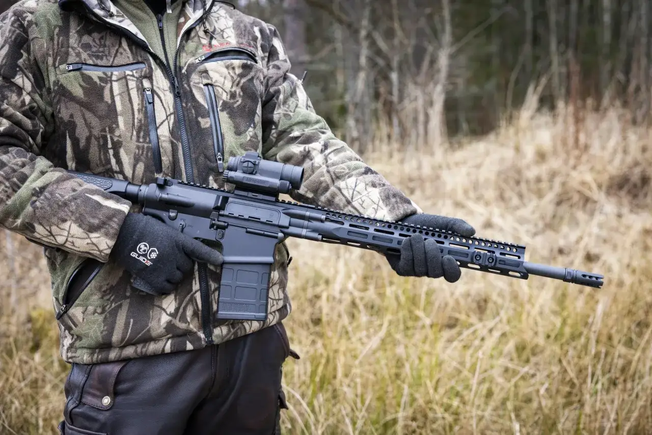 Person i kamouflagekl&auml;der h&aring;ller ett AR-15 gev&auml;r med kikarsikte, redo f&ouml;r ar 15 jakt i skogen.