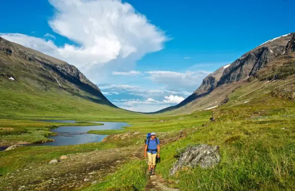 Vandrare på stig i en grön dalgång med sjö och fjäll. Syterskalet Hemavan bjuder på storslagen natur.