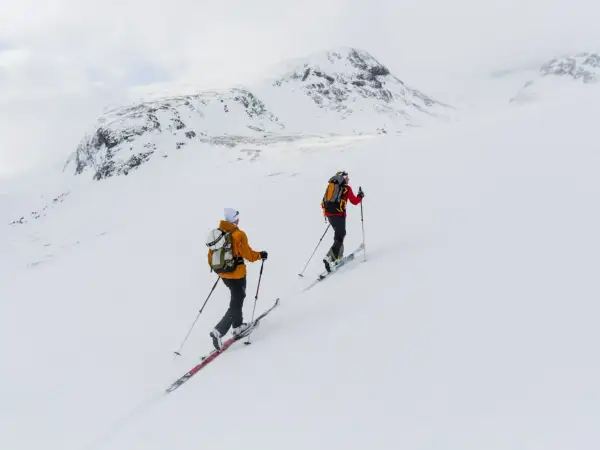 Två skidåkare på väg uppför ett snötäckt berg, en fantastisk sylarna topptur i fjällen.