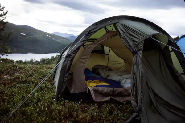 En öppen tält med sovsäckar redo för natten. En mysig känsla av värme i tält utan el, med en sjö och berg i bakgrunden.