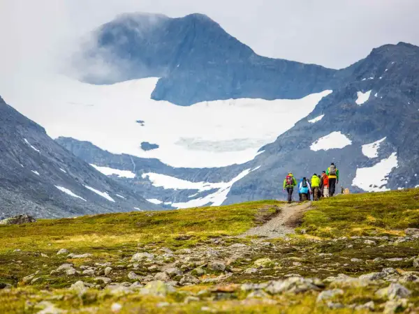 Vandrare på väg mot STF Sylarna, med glaciärklädda berg i bakgrunden.