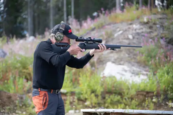Man med hörselskydd och keps siktar med ett Strasser RS700-gevär i skogen.